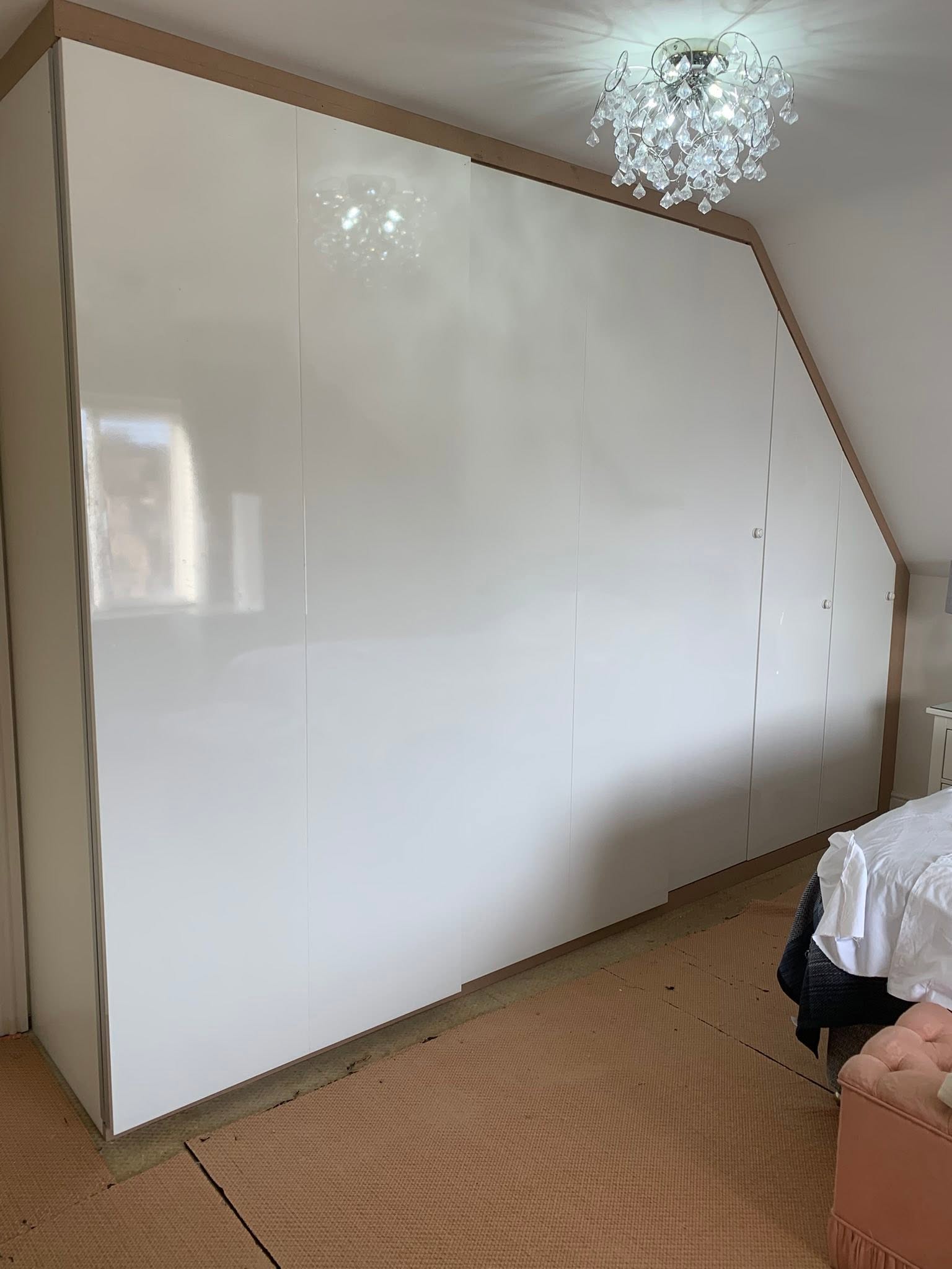 Gloss white sliding wardrobes fitted under a sloped ceiling